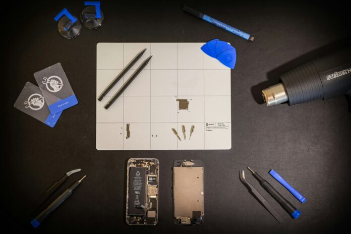 A phone, taken apart, lies on a black table with repair tools around it.