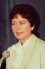 Anne Gorsuch stands in front of a microphone in a suit jacket. 