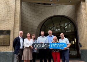 A group from the law firm Gould & Ratner stand with the firm’s black and blue sign in front of the firm’s new office in Denver.