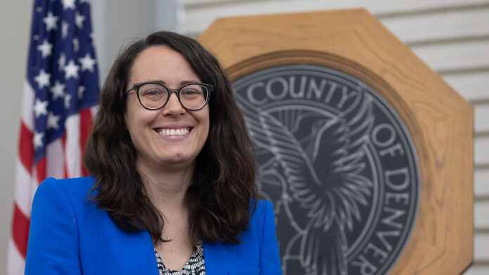 At-Large Denver City Council Member Sarah Parady stands in front of the seal of the City and Council of Denver.