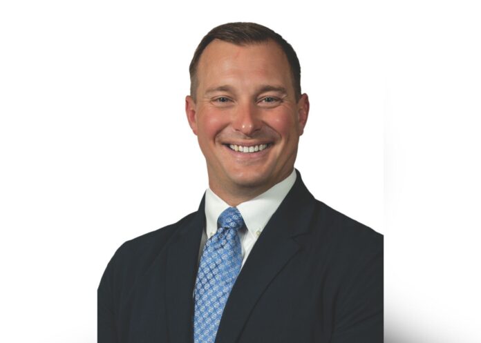 Benjamin Busboom smiles at the camera in a headshot photo, wearing a blue patterned tie and a navy suit jacket.