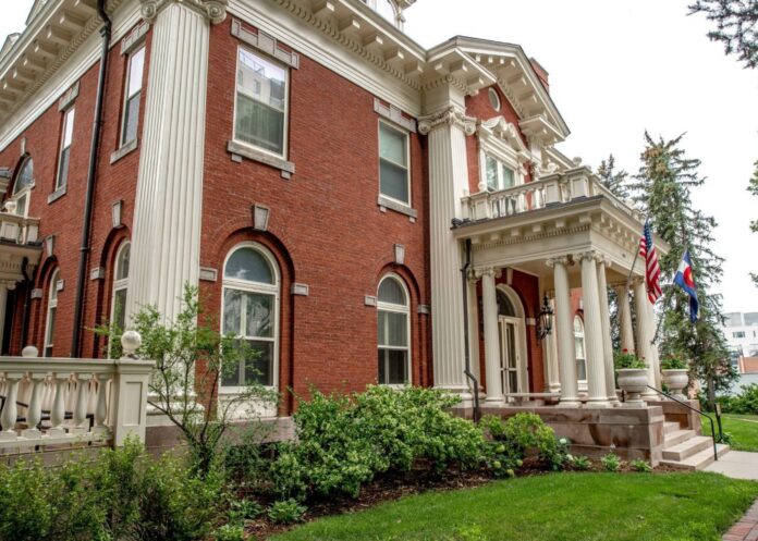 The front of Boettcher Mansion, the residence of the Colorado Governor, from a side angle. The exterior is of red brick, with several windows and columns in site.