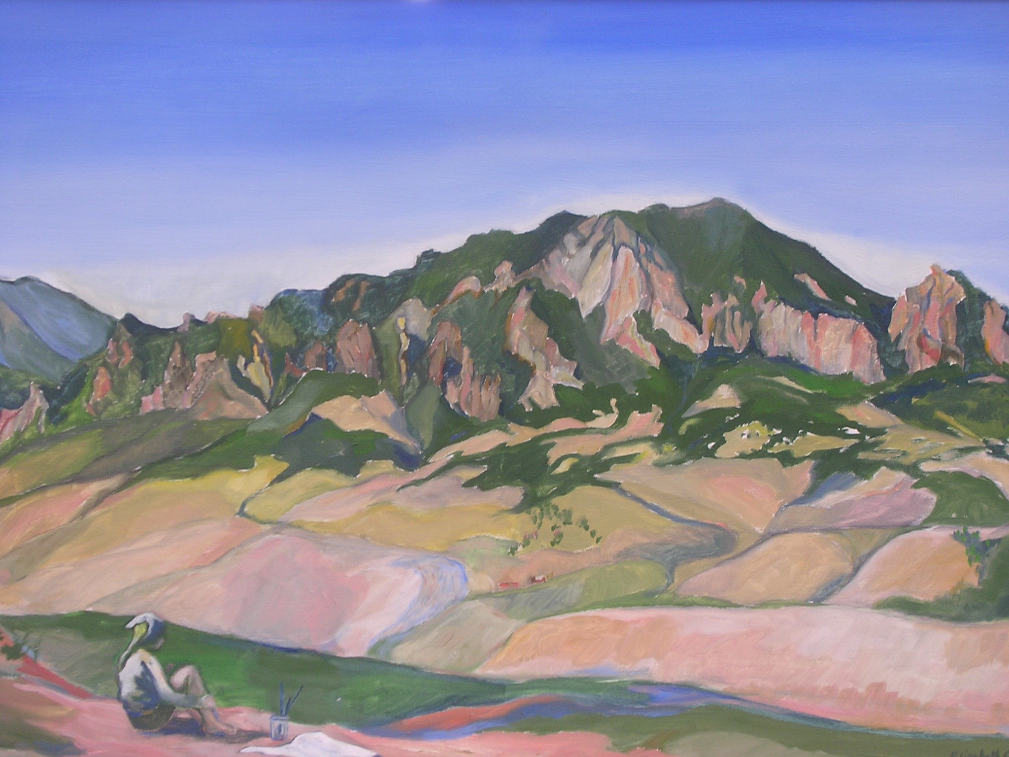 a green tipped mountain arcs high over land dotted with plants and a deep blue sky is spotless above. Someone sits on pink sandy ground in the foreground. It looks like a glass with painting supplies and a canvas rest on the ground next to them.