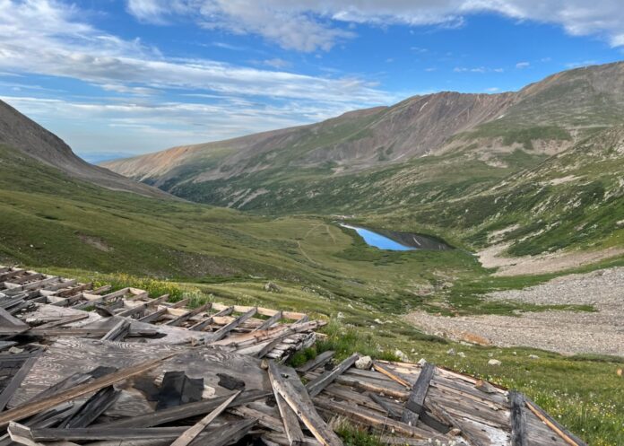 A green valley in the mountains with a lake in the center, with debris from an inactive mine in the foreground.