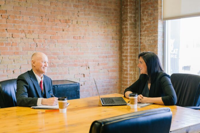 Two working professionals smile at each other in a meeting room.