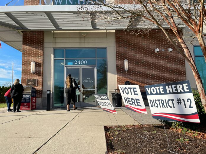 A polling center, with signs saying vote here and a woman at the front door.