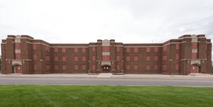 A long red brick building with grass in the foreground