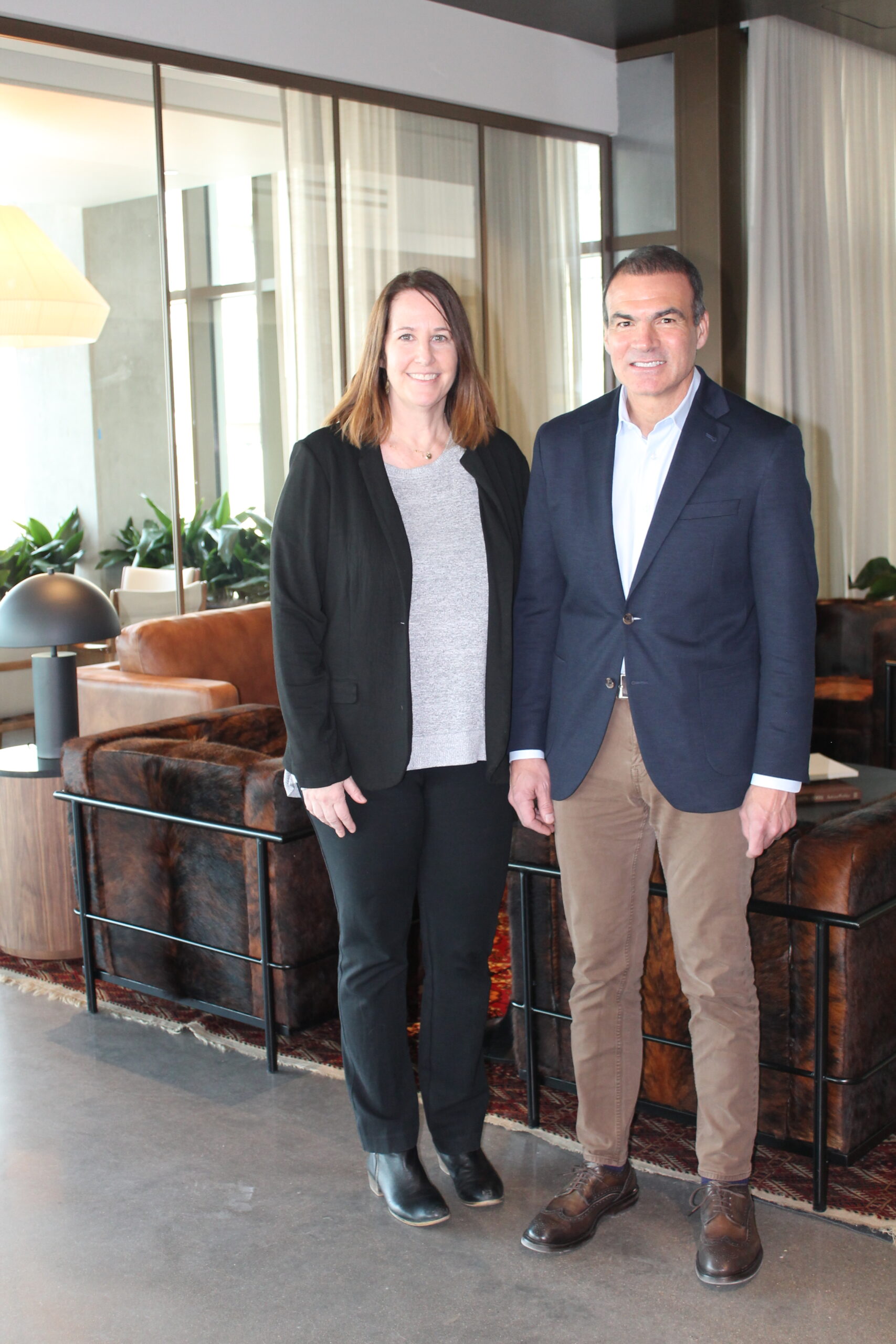 two people stand side-by-side in front of an office reception area